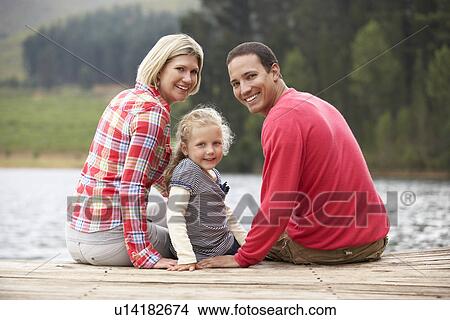 Young family sitting on a jetty View Large Photo Image Picture - Young family sitting on a jetty. Fotosearch
