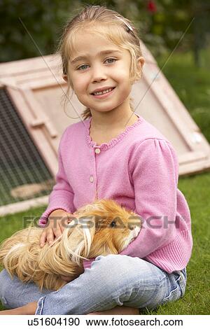 Stock Image - Young girl in garden holding guinea pig. Fotosearch