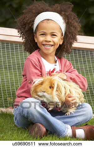 Stock Image - Young girl in garden holding guinea pig. Fotosearch