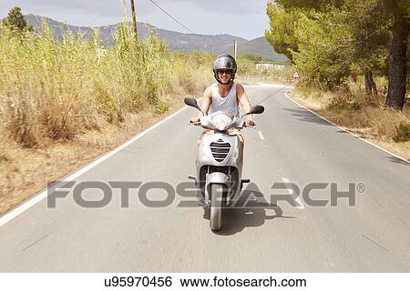 Stock Photograph - Young Man Riding Motor Scooter Along Country Road. Fotosearch