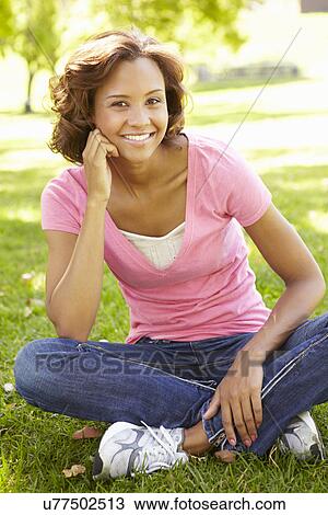Stock Image - Young woman sitting in park. Fotosearch