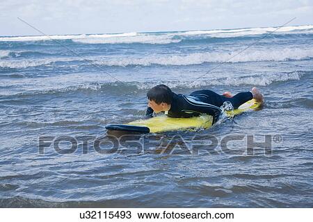 Boy lying on surfboard in water View Large Photo Image Stock Image - Boy lying on surfboard in water. Fotosearch