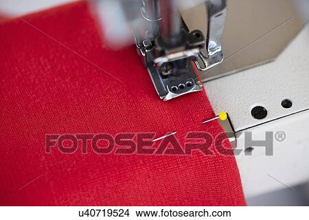 Picture - Close up of sewing machine and red textile in dressmakers workshop. Fotosearch