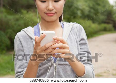 Stock Photography - Close up of young female runner selecting music from smartphone in park. Fotosearch