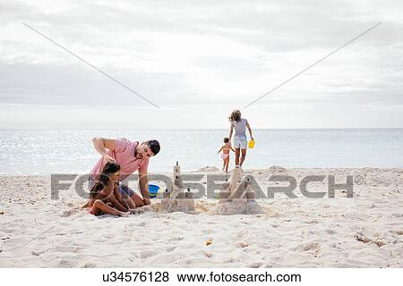 Stock Photo - Couple and two girls building sandcastle on beach, Tuscany, Italy. Fotosearch