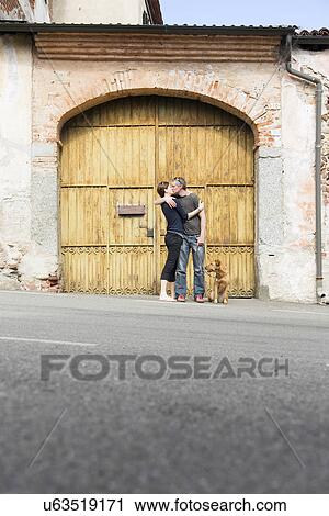 Stock Image - Couple kissing in front of building entrance on street, Suno, Novara, Italy. Fotosearch