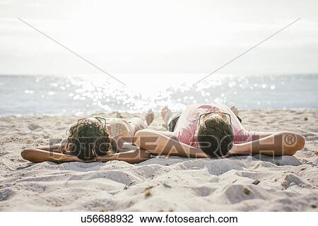 Stock Image - Couple lying on beach sunbathing, Tuscany, Italy. Fotosearch