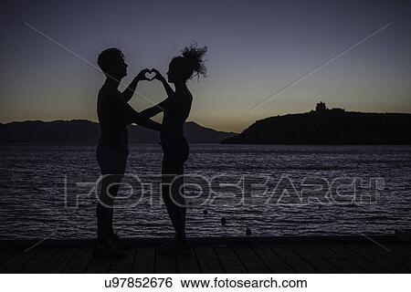Couple making heart shape with hands by sea, silhouette View Large Photo Image Stock Photograph - Couple making heart shape with hands by sea, silhouette. Fotosearch