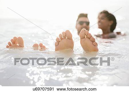 Stock Image - Couple with feet up in sea, Tuscany, Italy. Fotosearch