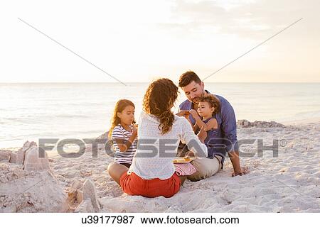 Stock Photo - Couple with two girls picnicing with cakes on beach, Tuscany, Italy. Fotosearch