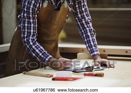 Stock Photograph - Cropped shot of mature craftsman making notes in organ workshop. Fotosearch