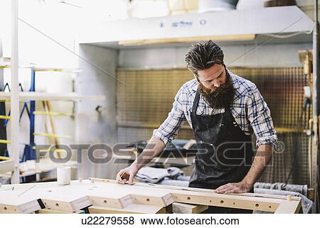 Stock Photo - Cropped shot of mid adult craftsman measuring wood in organ workshop. Fotosearch