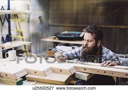 Stock Photo - Cropped shot of mid adult craftsman measuring wood component in organ workshop. Fotosearch