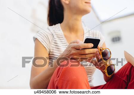 Stock Photograph - Cropped shot of mid adult woman holding sunglasses and smartphone, Tuscany, Italy. Fotosearch