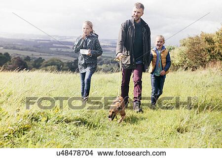 Picture - Father and two girls walking dog in field. Fotosearch