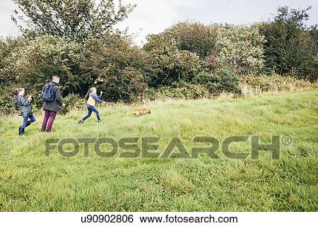 Stock Photograph - Father and two girls walking dog in field. Fotosearch