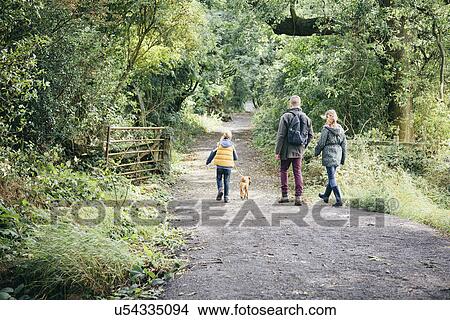 Picture - Father and two girls walking dog on rural road. Fotosearch