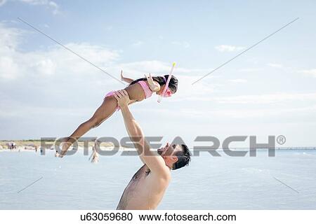 Stock Image - Father holding up snorkeler daughter in sea, Tuscany, Italy. Fotosearch