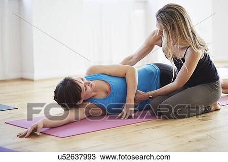 Stock Image - Female teacher holding stomach of student in pilates class. Fotosearch