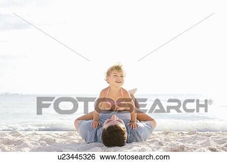 Stock Photograph - Female toddler sitting on top of father at beach, Tuscany, Italy. Fotosearch