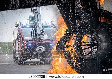 Stock Image - Fire engine spraying water on simulated fire at airport training facility. Fotosearch