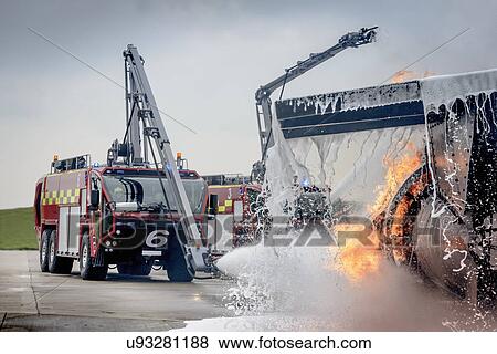 Stock Photo - Fire engine spraying water on simulated fire at airport training facility. Fotosearch