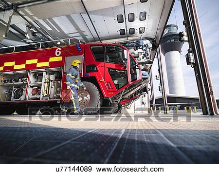 Stock Photo - Fireman carrying equipment to fire engine in airport fire station. Fotosearch