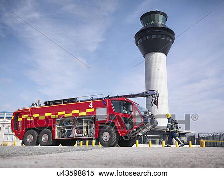Stock Photography - Fireman carrying equipment to fire engine in airport fire station. Fotosearch