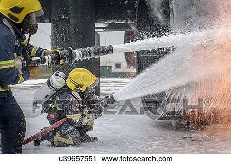 Stock Image - Firemen spraying water on simulated aircraft fire at training facility. Fotosearch
