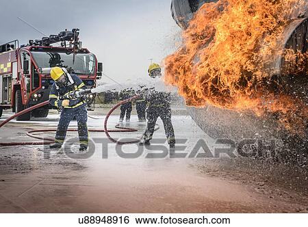 Stock Photograph - Firemen spraying water on simulated aircraft fire at training facility. Fotosearch