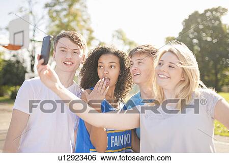 Stock Photograph - Four young adult basketball players taking smartphone selfie on court. Fotosearch