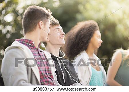 Four young adult friends sitting talking in park View Large Photo Image Stock Photo - Four young adult friends sitting talking in park. Fotosearch
