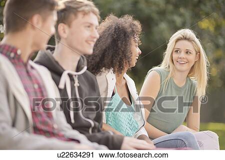 Four young adult friends talking in park View Large Photo Image Stock Image - Four young adult friends talking in park. Fotosearch