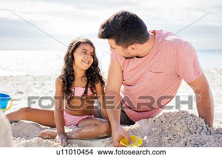 Girl and father building sandcastle on beach, Tuscany, Italy View Large Photo Image Picture - Girl and father building sandcastle on beach, Tuscany, Italy. Fotosearch