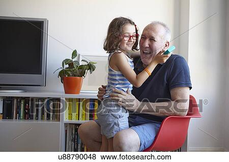 Stock Photo - Girl and grandfather laughing whilst playing hand held computer game. Fotosearch