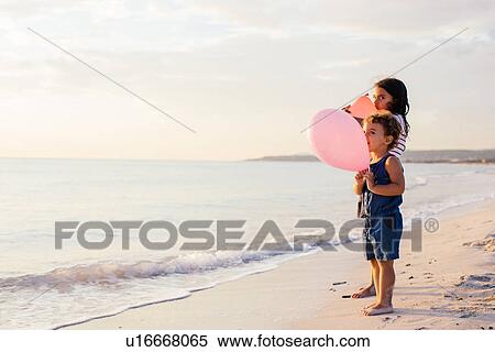 Stock Photography - Girl and toddler sister with balloons on beach, Tuscany, Italy. Fotosearch