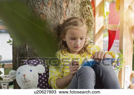 Stock Image - Girl with colouring book in tree house. Fotosearch