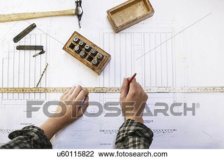 Stock Image - Hands of young craftswoman measuring blueprint in pipe organ workshop. Fotosearch