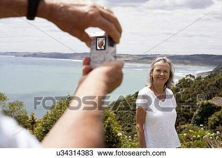 Stock Image - Husband photographing wife, ocean in background, Raglan, New Zealand. Fotosearch
