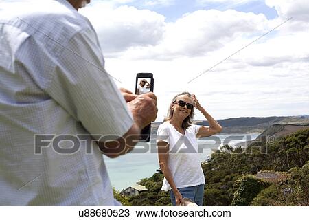Stock Image - Husband photographing wife, ocean in background, Raglan, New Zealand. Fotosearch