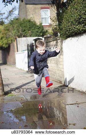 Male toddler in red rubber boots jumping into sidewalk puddle View Large Photo Image Picture - Male toddler in red rubber boots jumping into sidewalk puddle. Fotosearch
