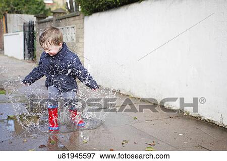 Male toddler in red rubber boots splashing in sidewalk puddle View Large Photo Image Stock Photo - Male toddler in red rubber boots splashing in sidewalk puddle. Fotosearch