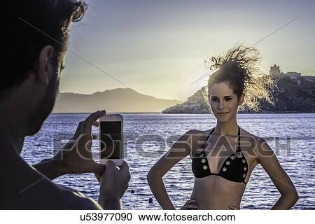 Stock Image - Man photographing young woman on vacation. Fotosearch