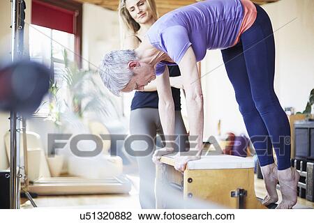 Mature Female Student Bending Over Combo Chair In Pilates Gym