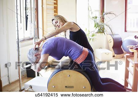 Stock Photography - Mature female student leaning forward onto pilates barrel in pilates gym. Fotosearch