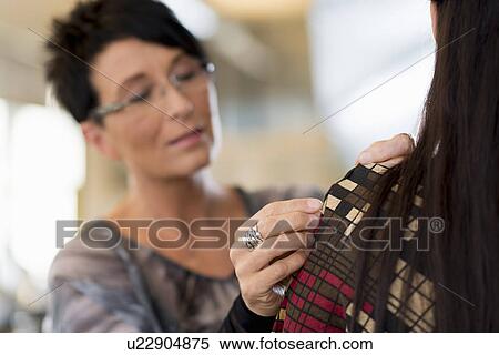 Stock Photography - Mature seamstress pinning shoulder of customers dress in workshop. Fotosearch