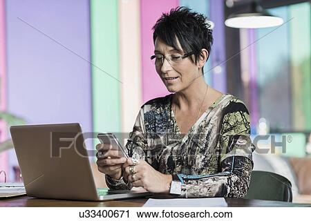 Mature seamstress reading texts on smartphone in workshop office View Large Photo Image Stock Image - Mature seamstress reading texts on smartphone in workshop office. Fotosearch