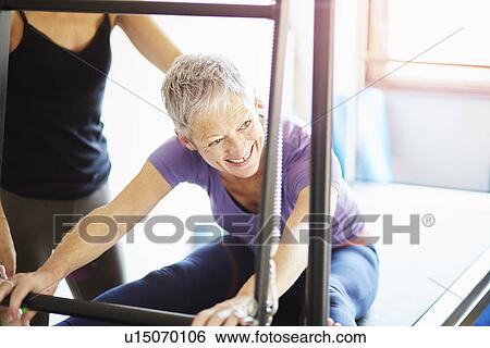 Stock Photograph - Mature woman and tutor practicing pilates on trapeze table in pilates gym. Fotosearch
