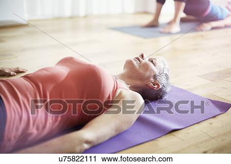 Stock Image - Mature woman lying on back in pilates class. Fotosearch