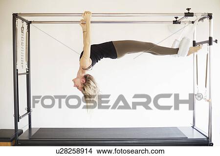 Picture - Mature woman practicing pilates on trapeze table in pilates gym. Fotosearch